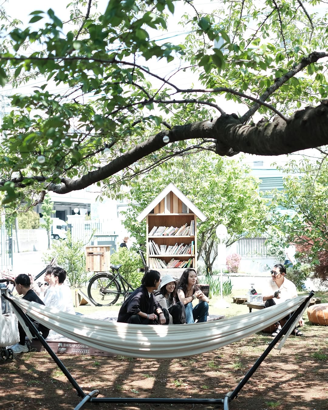 木陰のハンモックのそばに集い、会話を楽しむ人々